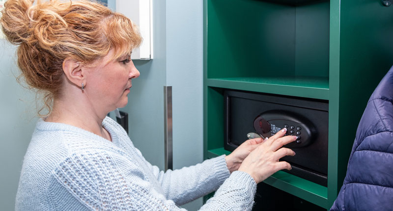 photo of a blonde woman placing items into a wall safe with a digital lock